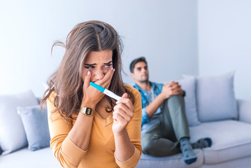 Upset woman looking in pregnancy test with her husband in background
