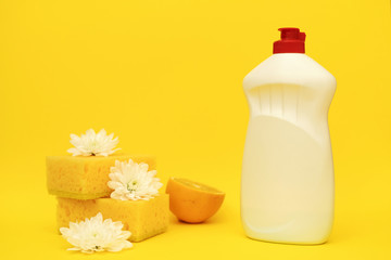 Pile of yellow polyurethane sponges laying near lemon, white flowers and bottle of soap
