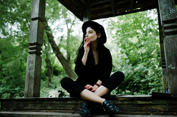 Sensual smoker girl all in black, red lips and hat. Goth dramatic woman smoking thin cigarette.