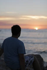 Young man sitting alone on the seashore during sunset. Warm, pleasant, summer evening on the Croatian coast. Calm end of the day on the shore. Vacation, rest in Croatia. Dusk, twilight, Adriatic Sea