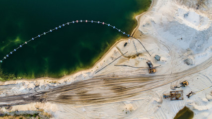 Aerial view of machinery and mine equipment near deep blue lake on sandy surface