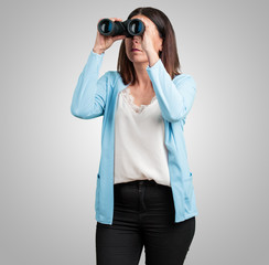 Middle aged woman surprised and amazed, looking with binoculars in the distance something interesting, concept of future opportunity