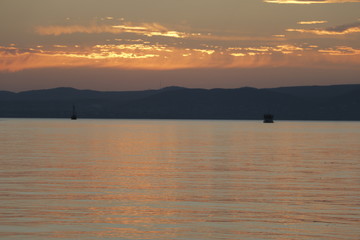 Two ships sailing on Lake Balaton. A warm, pleasant summer evening. A quiet end of the day. Beautiful sunset. Orange sky. Reflection of the sun on the surface of the water. Mountains in the background