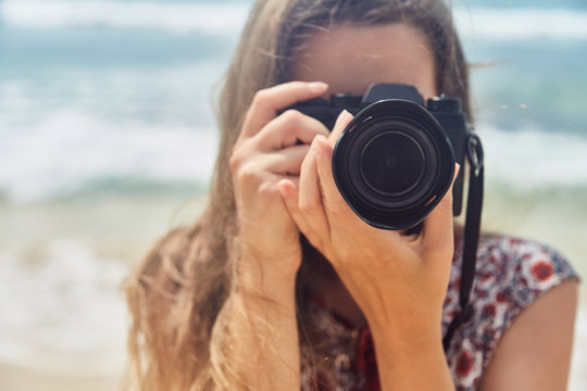young girl taking pictures on camera in a summer on the beach