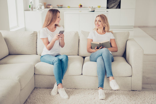 Close up photo of two people pretty mum mommy and teen daughter hands arms telephone diary sharing exchanging information love being together smiling wear white t-shirts jeans sit on comfy sofa