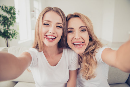 Close up photo of two people mum and teen daughter holding hands arms telephone funny tongue out of mouth make take selfie for dad daddy father wear white t-shirts jeans sit on comfy sofa