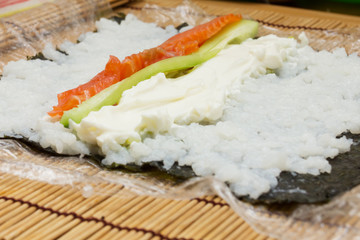 Homemade sushi. Male hands prepare rolls with rice, salmon, crab, cheese, nori, cucumber