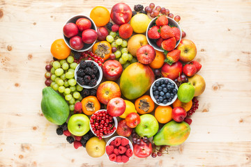 Rainbow fruits background circle, strawberries raspberries oranges plums apples kiwis grapes blueberries mango papaya on wooden table, top view, copy space for text, selective focus