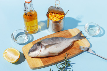Raw dorado fish on a wooden board, ingredients for cooking and spices on a blue background.