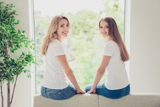 Close up back behind rear view photo two people mum and teen daughter best buddies hold arms motherhood parenthood wear white t-shirts jeans in bright flat sit comfortable sofa