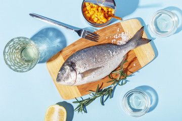 Raw dorado fish on a wooden board, ingredients for cooking and spices on a blue background.