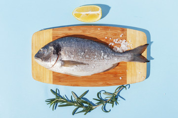 Raw dorado fish on a wooden board, ingredients for cooking and spices on a blue background.