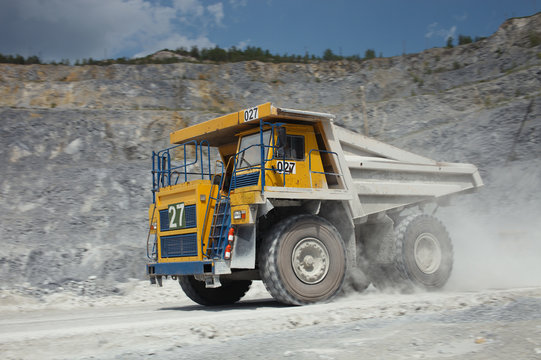 Large yellow mining truck is ride at high speed in a limestone quarry closeup. Mining industry.