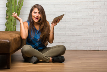 Portrait of young latin woman sitting on the floor crazy and desperate, screaming out of control,...