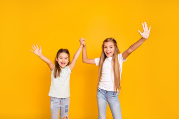 Portrait of two nice cool crazy attractive lovely cheerful cheery positive girlish girls holding hands having fun isolated over bright vivid shine yellow background
