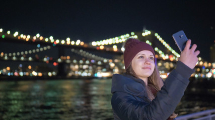 Girl takes a selfie photo at Brooklyn Bridge by night