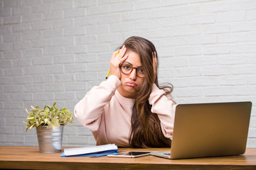 Portrait of young student latin woman sitting on her desk frustrated and desperate, angry and sad with hands on head