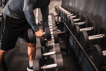 Close-up image of muscular man picking heavy dumbbell in the gym.
