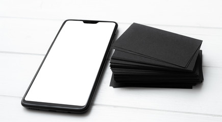 Blank of modern smartphone and black business cards stack on white table for your design