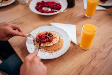 Eating pancakes with raspberries and drinking juice on wooden table.