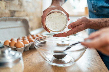 Close-up image of man adding flour into glass bowl. Couple baking together.