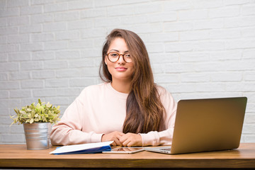 Portrait of young student latin woman sitting on her desk cheerful and with a big smile, confident, friendly and sincere, expressing positivity and success