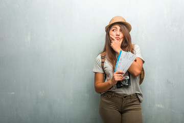 Portrait of young traveler latin woman against a wall doubting and confused, thinking of an idea or worried about something. Holding a boarding pass.