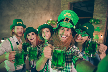 Group buddies arms raise beverage wear specs eyewear eyeglasses national culture costumes tradition hats checkered plaid jeans shirts lucky leaf false beard laugh laughter make take selfies