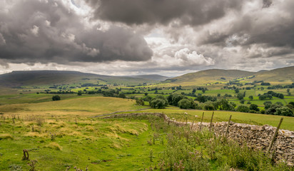 Fototapeta na wymiar storm clouds gathering over a valley of farm land in Yorkshire, England. Handmade stone wall. Sheep grazing. 