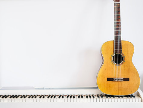 Acoustic guitar on piano keyboard in front of white wall.