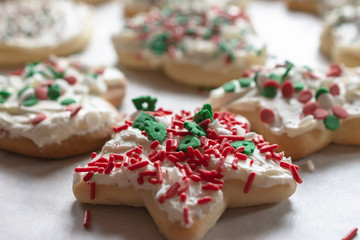 Close up view of star shaped sugar cookies with frosting and sprinkles.  Additional christmas cookies in various shaped blurry in the background.