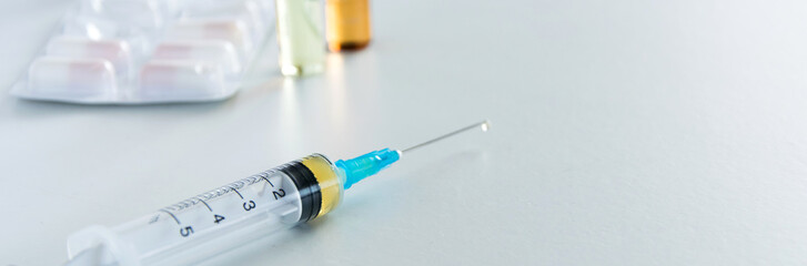 Medical syringe with injection solution, medicine pills and capsules on white background. Healthy medical concept