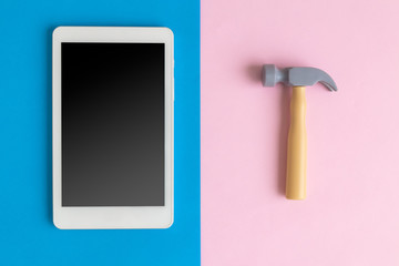 Flat lay of digital tablet and hammer toy against pastel background.