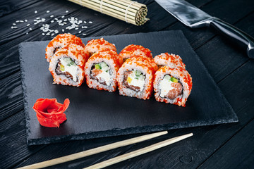 Served sushi rolls on black stone with chopsticks. Close up view on sushi on dark background. Traditional japanese cuisine. Restaurant, food menu, recipe, cafe concept. Lifestyle with copy space