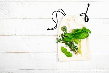 Bunch of fresh basil and rosemary on a white cotton eco bag on a white wooden background. The concept of no plastic zero waste house shopping. Copy space. Top view.