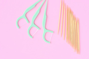Plastic green toothpicks with dental floss for personal daily teeth hygiene and wooden bamboo tooth picks on pink background. Dentistry tooth pick with thread for interdental oral care