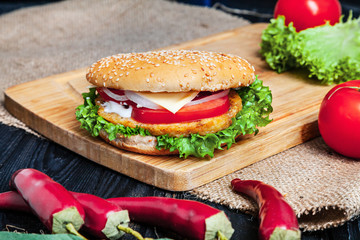 Chicken Burger with meat, sauce and vegetables on on wooden background. Close up view on american fast food. Restaurant, food menu, recipe, cafe concept. Lifestyle with copy space