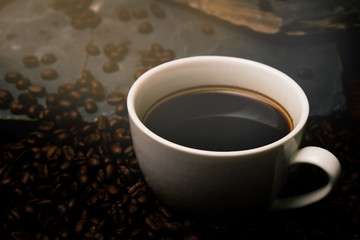 Cup of coffee with smoke and coffee beans on table with coffee beans.