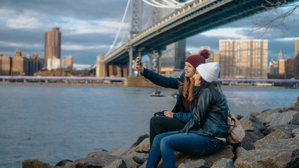 Two girls sit at Manhattan Bridge and enjoy their sightseeing trip to New York
