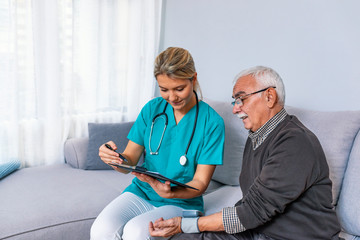 Happy senior man having his blood pressure measured in a nursing home by her caregiver. Happy nurse...