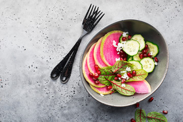Healthy food. Watermelon radish, cucumber, rice, pomegranate seeds, sorrel, red veins salad in a bowl on a dark background. Top view. Copy space.