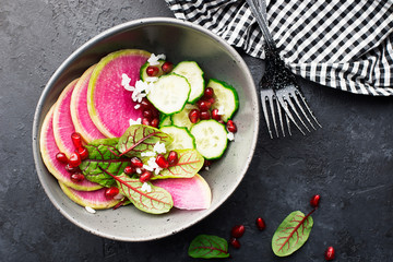 Healthy food. Watermelon radish, cucumber, rice, pomegranate seeds, sorrel, red veins salad in a bowl on a dark background. Top view. Copy space.