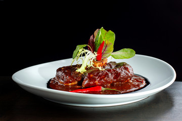 Meat with hot pepper sauce laid out on a white plate.