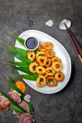 Fried squid rings on white plate decorated with tropical leaves. Gray concrete background, top view