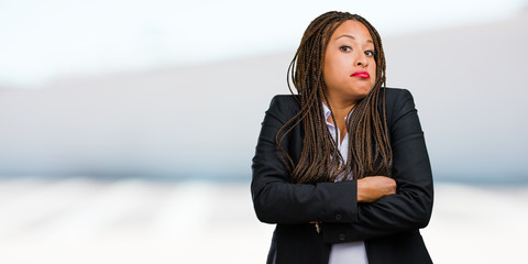 Portrait of a young black business woman doubting and shrugging shoulders, concept of indecision and insecurity, uncertain about something - obrazy, fototapety, plakaty