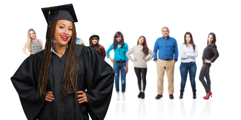 Young graduated black woman wearing braids with hands on hips, standing, relaxed and smiling, very positive and cheerful