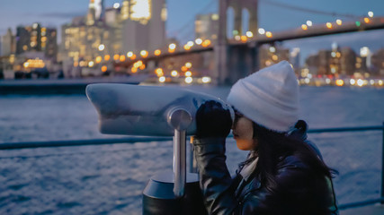 Young woman looks through a spyglass at Brooklyn Bridge New York