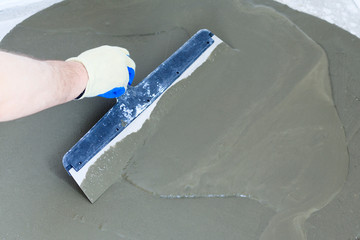 concrete floor. on it fly out to even out the horizon. close-up. worker with a spatula to drive the liquid across the floor