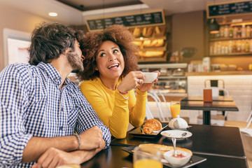 Young couple at cafe, the guy is whispering her and she is surprised.