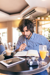 Young modern man having a breakfast at cafe, writing in a notebook, thinking about a great idea.